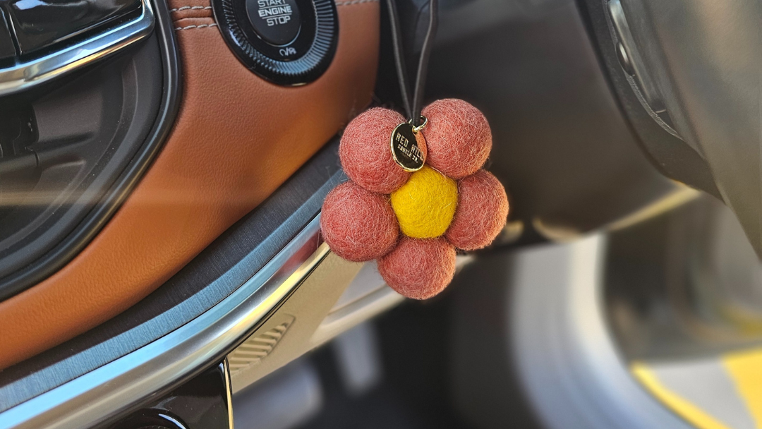 Red Hill Candle Co. red felt flower air freshener hanging in the car