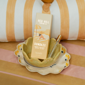 Perfume bottle with 'Red Hill Perfume Co' packaging on a decorative dish with striped background